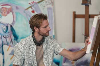 Artist creating a colourful mixed media painting using acrylic paint, collage and drawing materials."